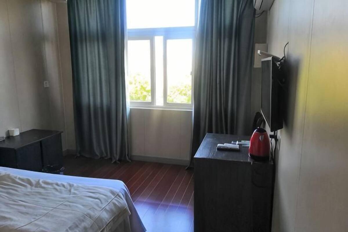 Een hotelkamer met een bed, een bureau, een stoel, een raam met gordijnen en een aan de muur bevestigde televisie.