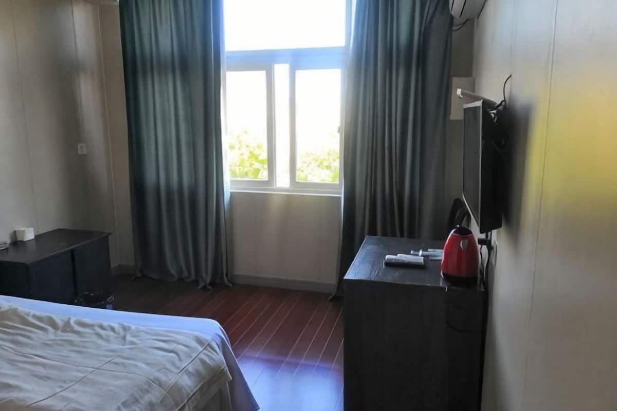 A hotel room with a bed, a desk, a chair, a window with curtains, and a wall-mounted TV.