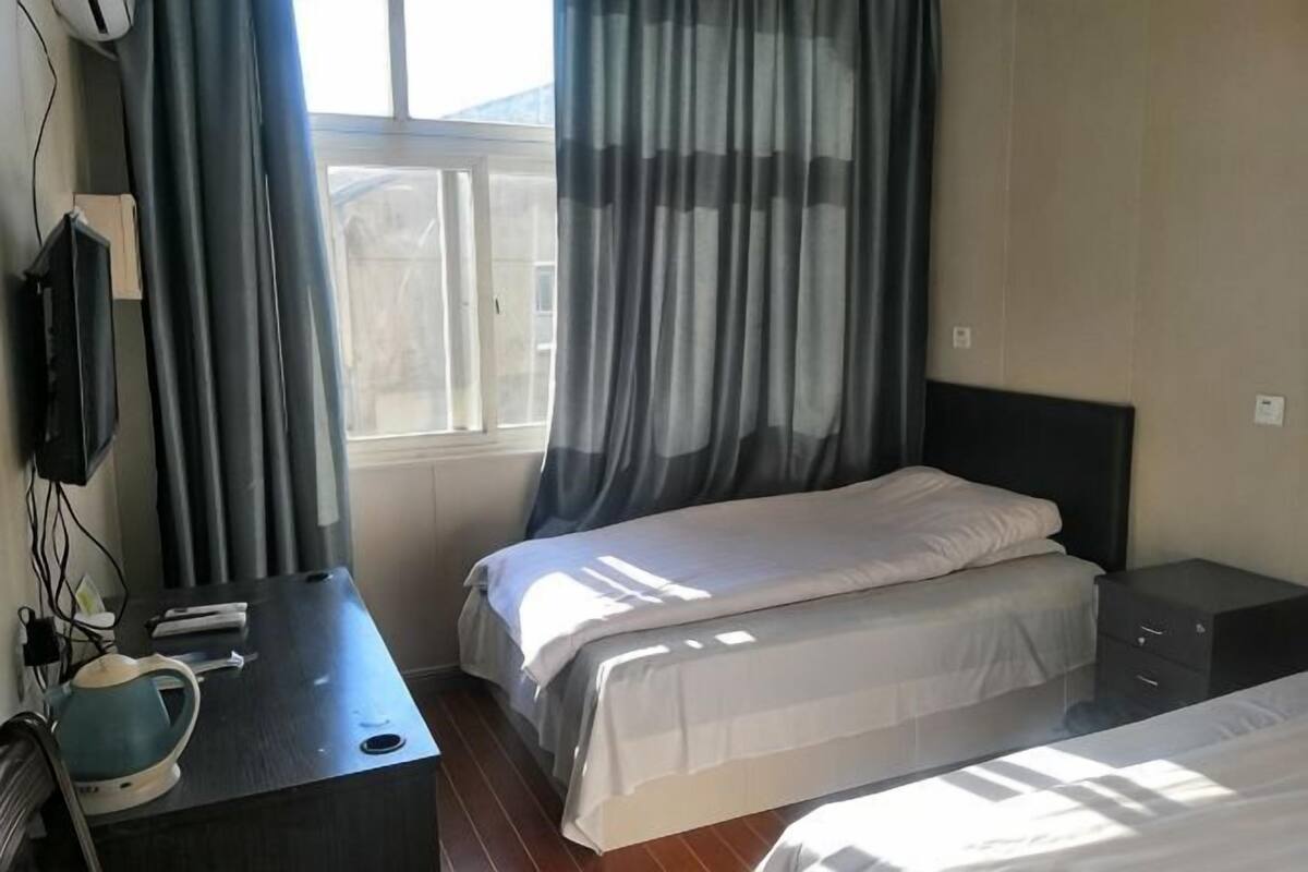 Een hotelkamer met twee bedden, een bureau met stoel, een televisie en een raam met gordijnen.