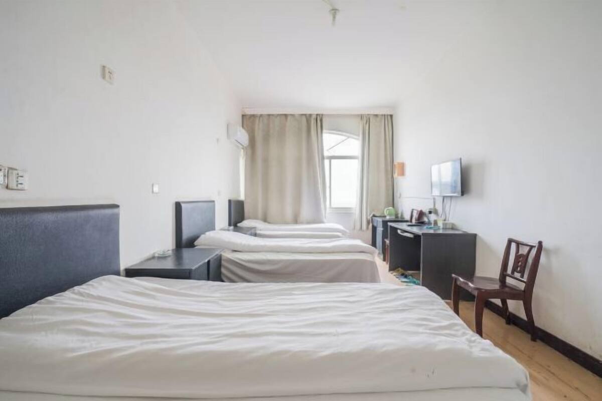 Een hotelkamer met twee éénpersoonsbedden, een bureau met stoel, een televisie en een raam met gordijnen.