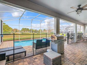 Un espacio al aire libre techado con piscina, estación de parrillada y zona de estar.