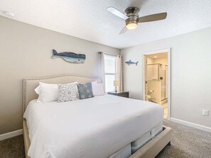 A bedroom with a bed, a ceiling fan, and a door leading to a bathroom.