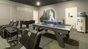 Um quarto com mesa de pebolim, duas cadeiras, mesa de bilhar e um mural na parede.