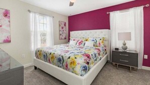 Quarto com cama, mesa de cabeceira, ventoinha no teto e janela com cortinas.