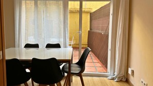 A dining area with a table and chairs, a sliding glass door leading to a patio with a yellow wall and a wooden fence. - 2 BEDROOM DUPLEX (Barcelona)