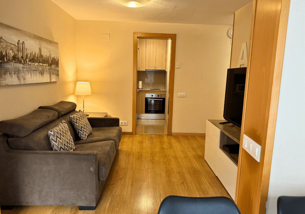 A compact living space with a sofa set, a television, and a kitchenette.