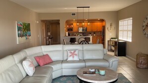 A living room with a sectional sofa, a round coffee table, and a kitchen in the background. - Luxury Penthouse Bella Lago 441 (Fort Myers Beach)