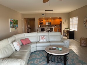 A living room with a sectional sofa, a round coffee table, and a kitchen in the background.