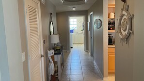 A hallway with a ceiling light, a door with a window, a wall-mounted lamp, and a decorative wall piece. - Luxury Penthouse Bella Lago 441 (Fort Myers Beach)