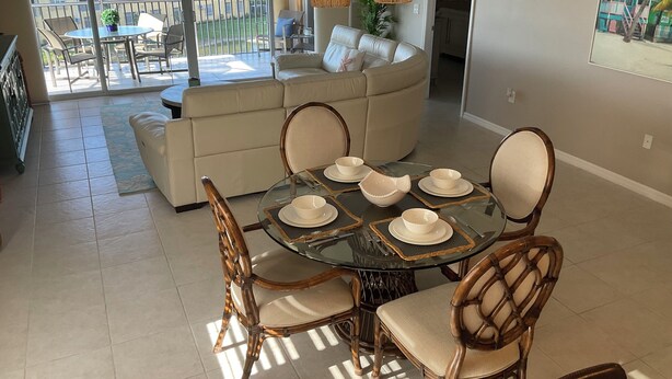 A dining area with a glass table, wicker chairs, and a sofa in the background. - Luxury Penthouse Bella Lago 441 (Fort Myers Beach)