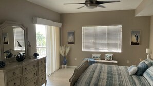 A bedroom with a bed, dresser, vanity, ceiling fan, window with blinds, and wall art. - Luxury Penthouse Bella Lago 441 (Fort Myers Beach)
