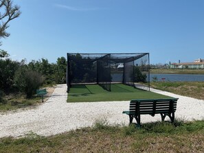 Un terrain de sport entouré d’un filet, avec un banc et un chemin de gravier.