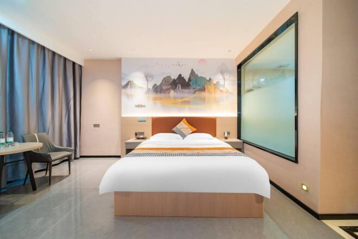 Une chambre d’hôtel avec un grand lit, un bureau avec une chaise, une table de chevet et une grande fenêtre.