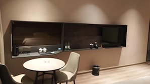 Ein modernes Hotelzimmer mit einem runden Esstisch, zwei Stühlen, einer kleinen Bar mit Fernseher und einem Mülleimer.
