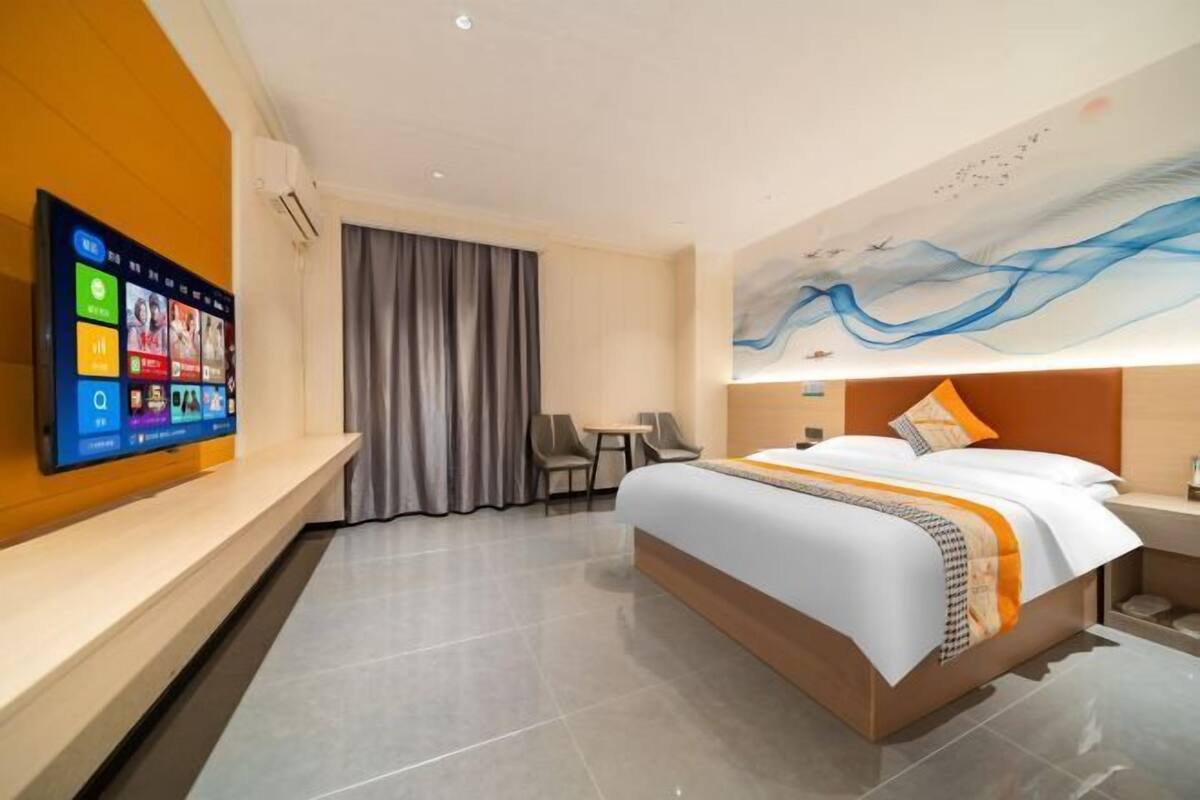 Une chambre d’hôtel moderne avec un grand lit, un téléviseur à écran plat fixé au mur, une petite table avec des chaises et un tableau au mur.