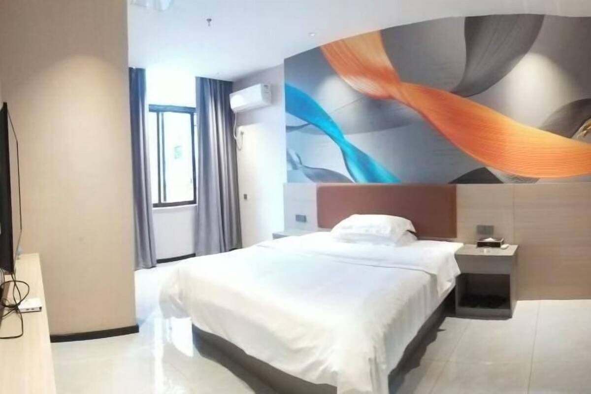 Une chambre d’hôtel comprenant un lit, une table de chevet, un climatiseur fixé au mur et une fenêtre avec des rideaux.
