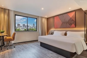 Habitación de hotel con una cama grande, un escritorio, una silla, una ventana con vista a la ciudad y un cuadro abstracto moderno en la pared.