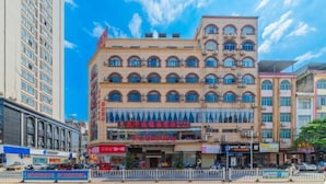 Ein mehrstöckiges Hotel mit zentralem Eingang, mehreren Balkonen und blauem Himmel.