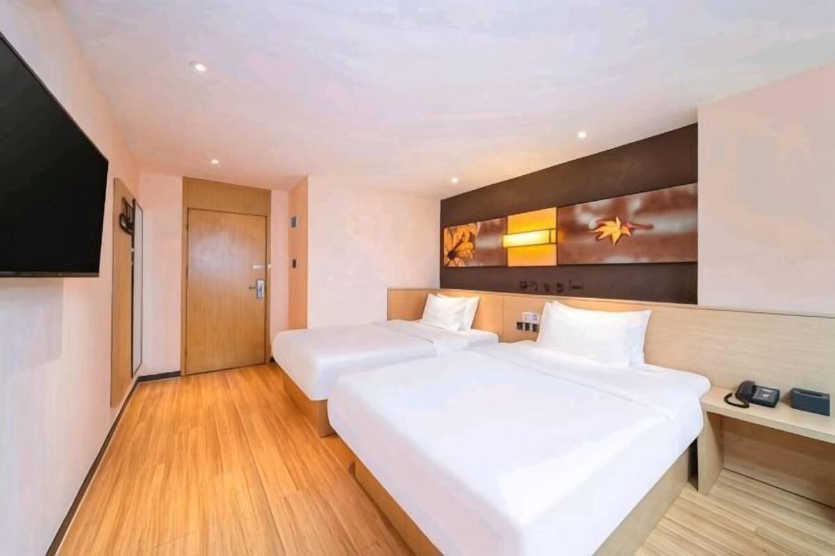 Une chambre d’hôtel avec deux lits, un plancher en bois, un téléviseur à écran plat et une œuvre d’art accrochée au mur.