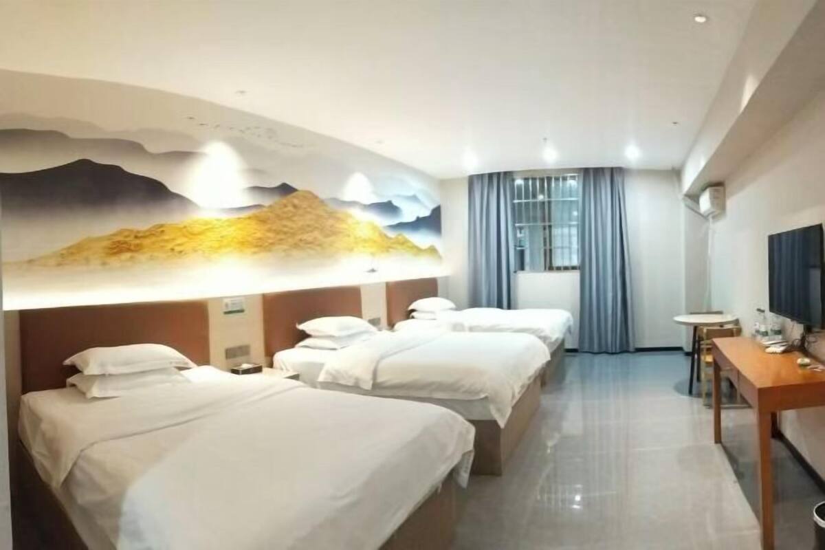 Une chambre d’hôtel avec trois lits, un bureau, une télévision et une grande fresque murale.