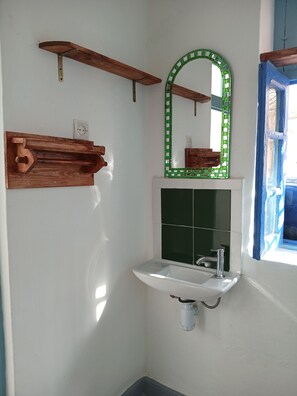 A bathroom with a white sink, green-tiled wall, wooden shelves, and a green-framed mirror. - Charming apartment in the heart of the old city near the beach (Essaouira)