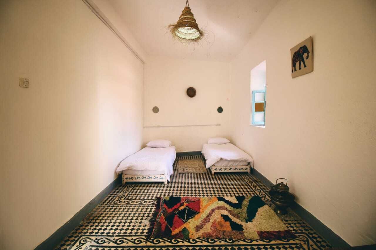 Habitació amb dos llits, un paviment amb dibuixos, una làmpada penjant i una finestra petita que dona a una vista.