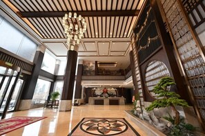 A hotel lobby with a reception desk, a chandelier, and a large window. - Qixian Hotel (Qi County)