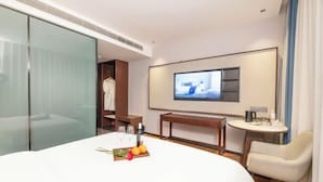 A hotel room with a large bed, a TV mounted on the wall, a small table with a bottle and glasses, and a chair. - Qixian Hotel (Qi County)
