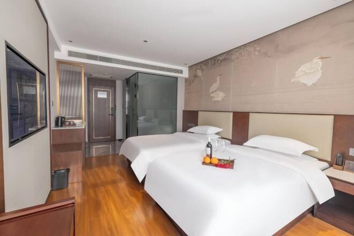 Habitación de hotel con una cama grande, una mesita de noche pequeña, un espejo y una pared con un panel decorativo.
