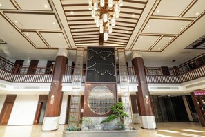 A spacious lobby with a modern chandelier, a central decorative wall, and a staircase. - Qixian Hotel (Qi County)
