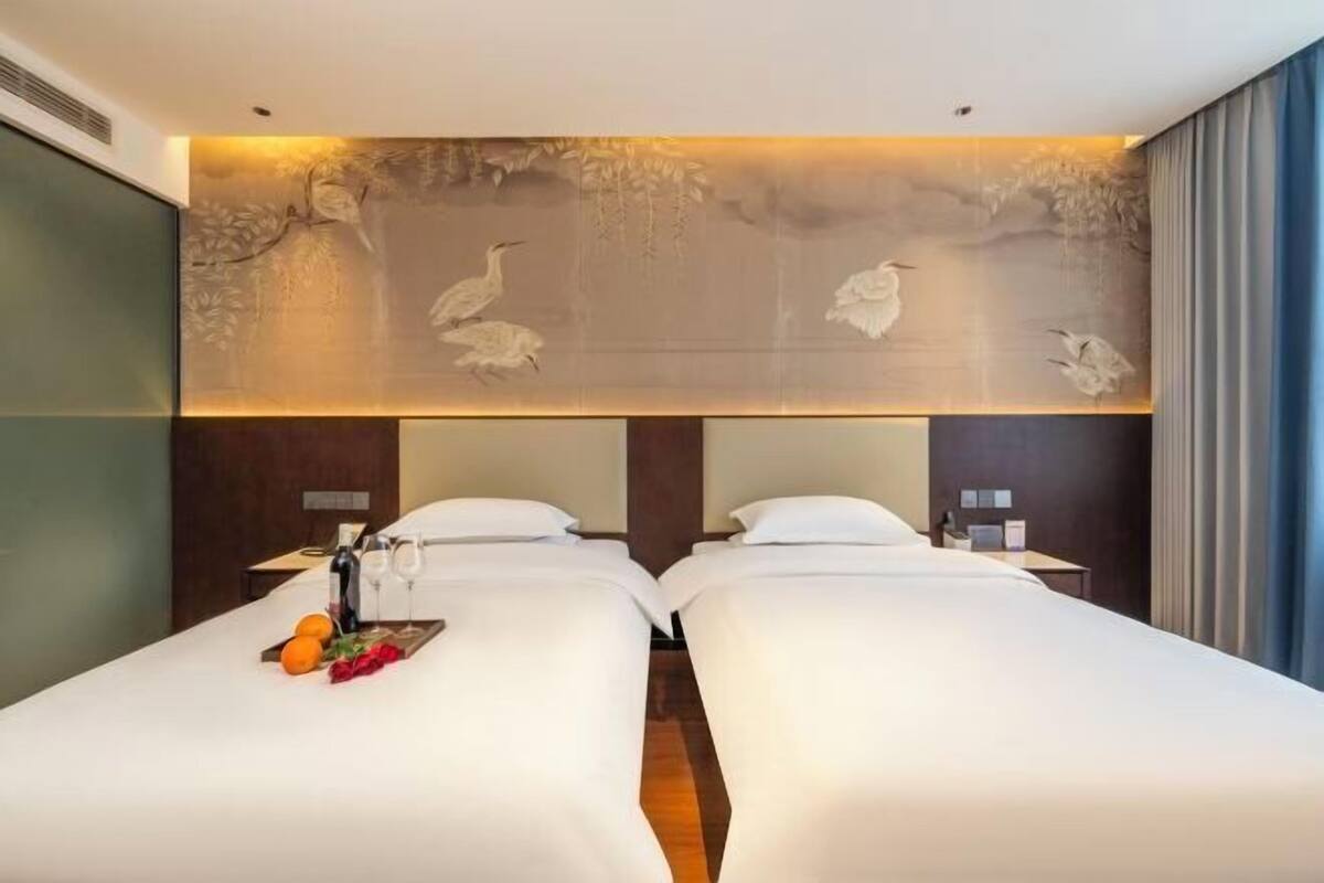 Habitación de hotel con dos camas, un mural en la pared y vista al mar.