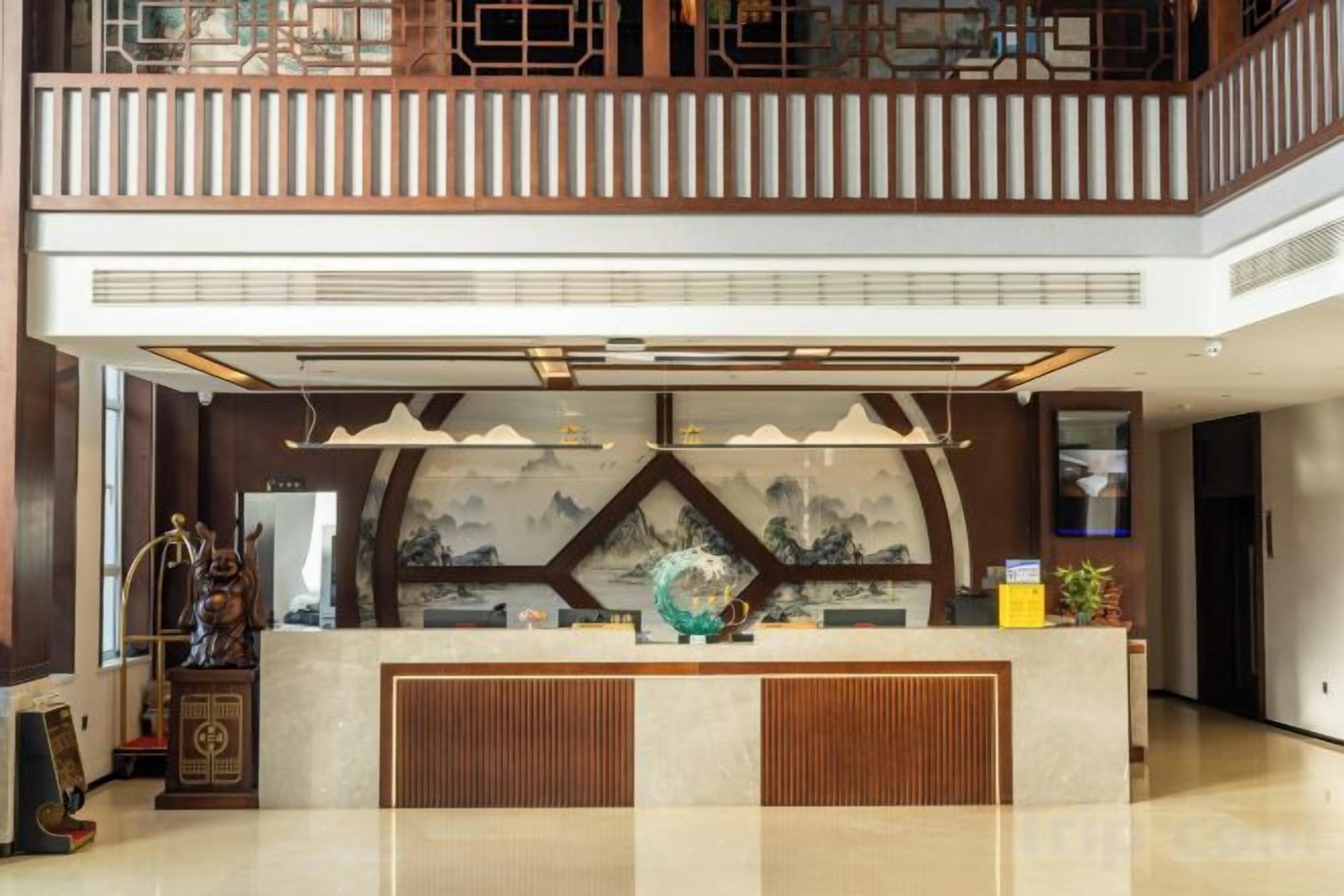 A hotel lobby with a reception desk, a decorative wall with artwork, and a balcony with railings.