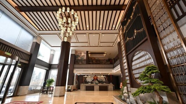 A spacious lobby with a reception desk, a chandelier, and a decorative wall with a bonsai tree. - Qixian Hotel (Qi County)