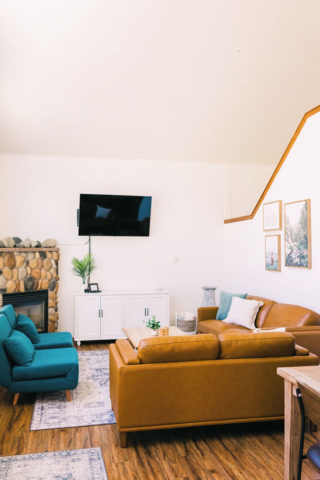 A living room with a stone fireplace, a television mounted on the wall, a white cabinet, and a brown sofa.