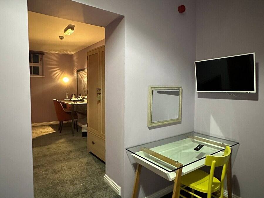 A small room with a glass table, a chair, a television mounted on the wall, and a door leading to another room.
