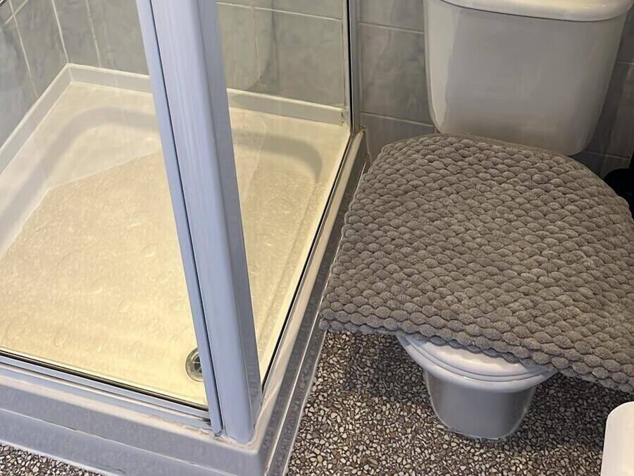 Un baño con cabina de ducha de vidrio, inodoro y una alfombra pequeña.