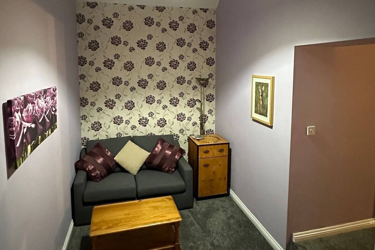 A small, cozy living room with a grey sofa, a wooden coffee table, and patterned wallpaper.