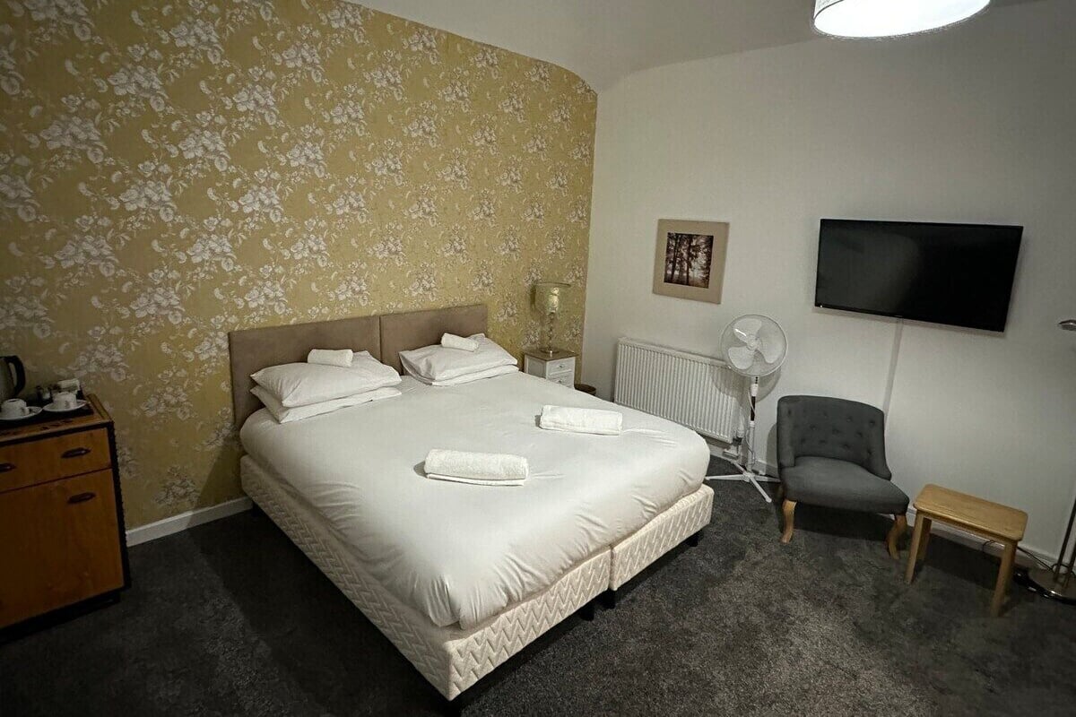 A neatly arranged bedroom with a bed, bedside table, lamp, chair, and a television mounted on the wall.