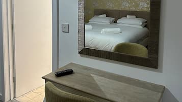 A hotel room with a bed, a desk with a chair, a mirror, and a door.