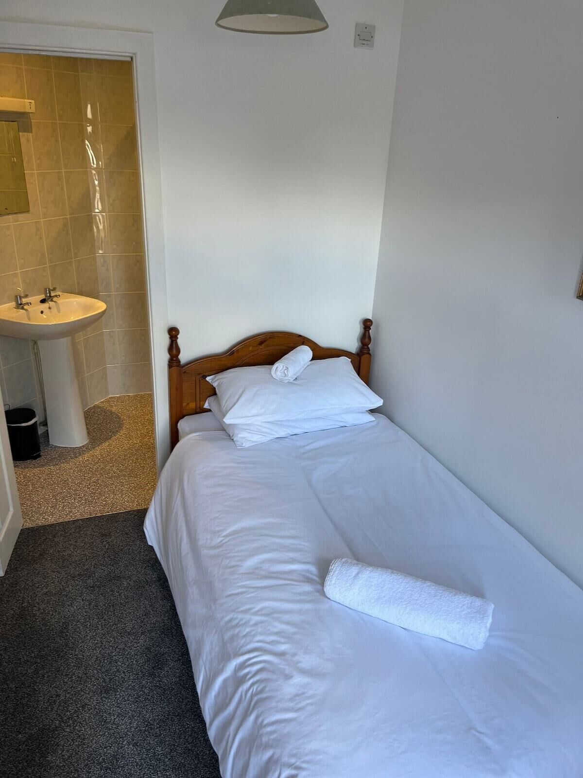 A small, clean room with a single bed, a white sink, and a shower area.