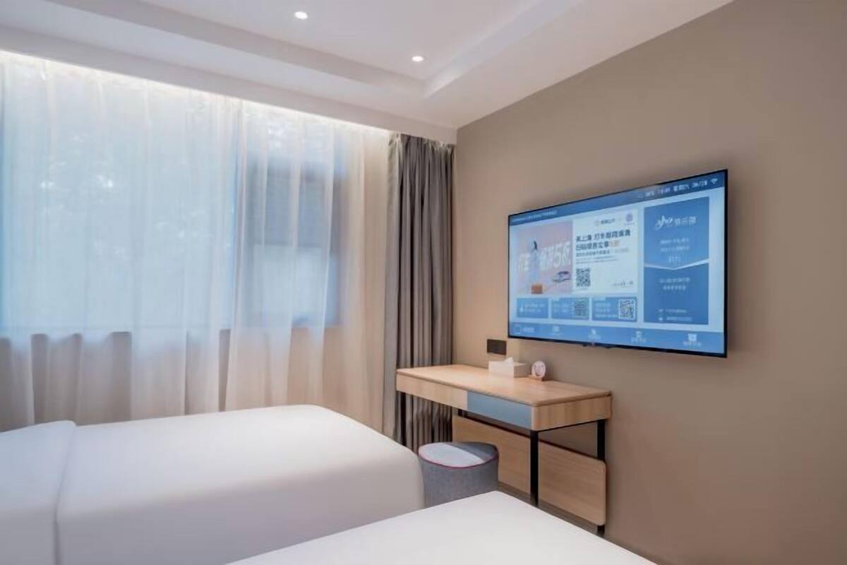 A hotel room with two beds, a desk, and a large screen displaying information.