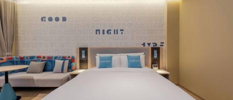A hotel room with a large bed, a sofa, a small table, and a wall with text patterns.