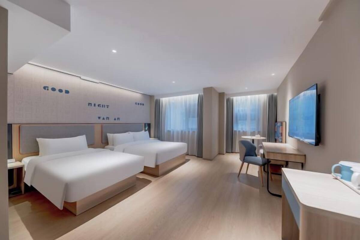 A modern hotel room with two beds, a desk, and a TV.