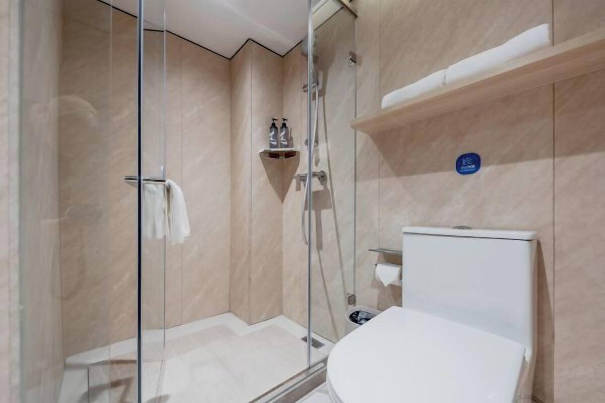 A modern bathroom with a glass shower enclosure, a white toilet, and a shelf with toiletries.