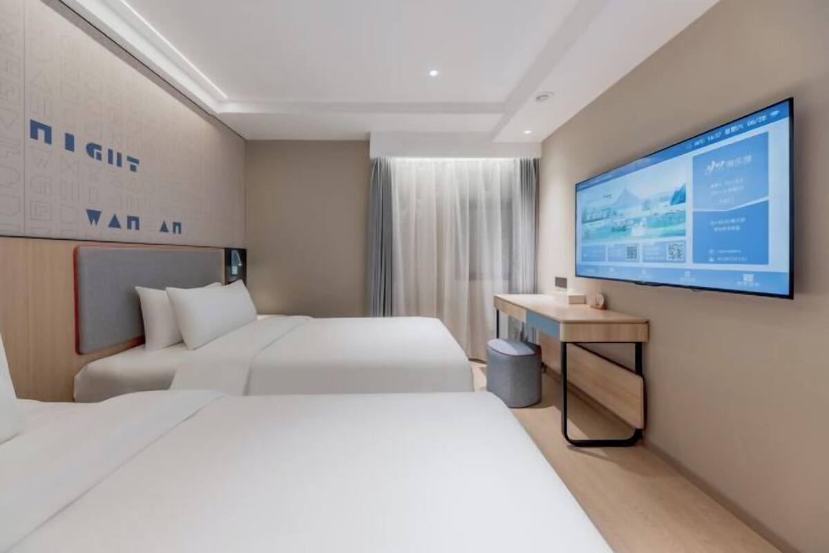 A hotel room with two beds, a desk, a television, and a window with curtains.