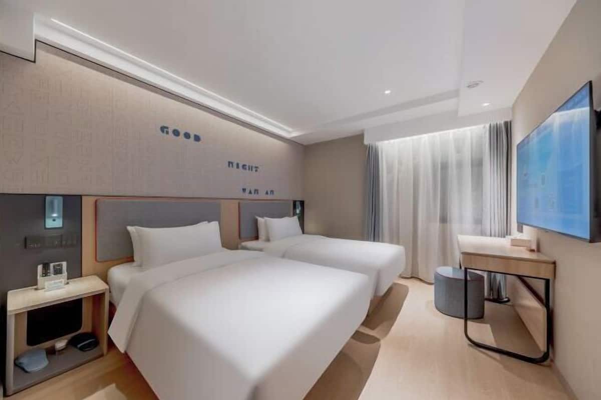 A hotel room with two beds, a desk, a chair, a TV, and a window with curtains.