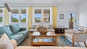 Ein Wohnzimmer mit einer Couch, Sesseln, einem Couchtisch und Blick ins Freie durch große Fenster.