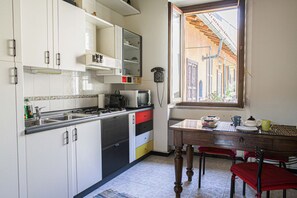 A kitchen with white cabinets, a microwave, a stove, and a window with a view of buildings. - VICOLO LAVANDAI - Petit Apartment Navigli (Milano)