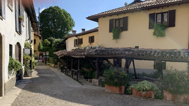 Ruada de calçada estreita, flanqueada por edifícios tradicionais, alguns com varandas e plantas em vasos.