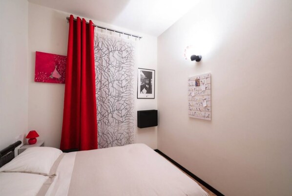 A bedroom with a bed, a red curtain, a wall-mounted TV, and a bulletin board. - VICOLO LAVANDAI - Petit Apartment Navigli (Milano)